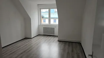 Helles Schlafzimmer im Dachgeschoss mit Laminatboden, Dachschrägen und einem Fenster mit Ausblick.