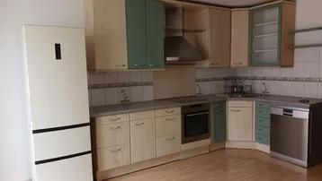 Einbauküche mit hellen Holzschränken, grünen Akzenten und modernen Geräten.
