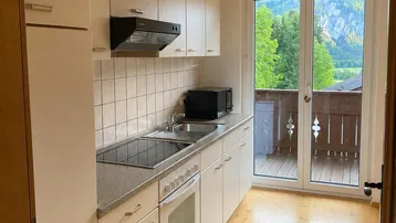 Funktionale Küche mit weißen Schränken, Holzboden und Zugang zu einem Balkon mit Bergblick.