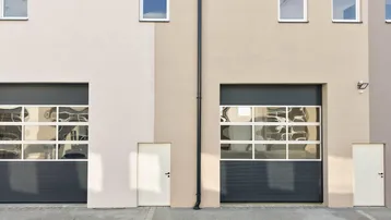 Fassade eines modernen Gebäudes mit zwei großen Garagentoren und separaten Eingangstüren.