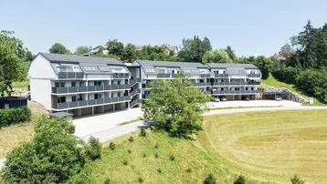 Moderne Wohnanlage mit mehreren Balkonen und umliegender Grünfläche unter blauem Himmel.