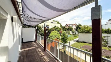 Geräumiger Balkon mit Holzboden, Markise und Blick auf den grünen Innenhof mit Spielplatz.