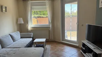 Gemütliches Wohnzimmer mit großem Ecksofa, Fliesenboden und Zugang zum Außenbereich.