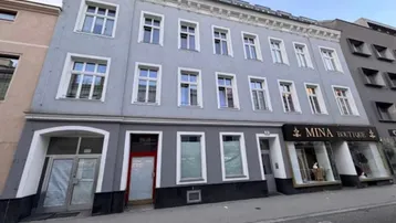 Ansicht eines mehrstöckigen Gebäudes mit Geschäften im Erdgeschoss und Wohnungen darüber.