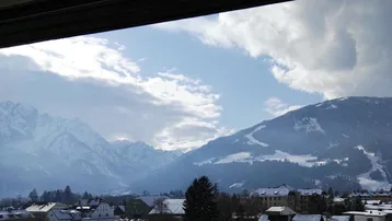 Panoramablick auf schneebedeckte Berge und eine verschneite Stadtlandschaft unter bewölktem Himmel.