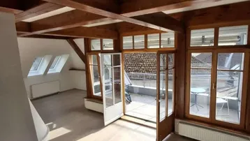 Helles Wohnzimmer mit sichtbaren Holzbalken, Kamin und Zugang zu einer sonnigen Terrasse.