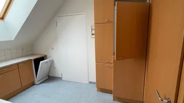 Küche im Dachgeschoss mit Holzschränken, Dachfenster und integriertem Geschirrspüler.