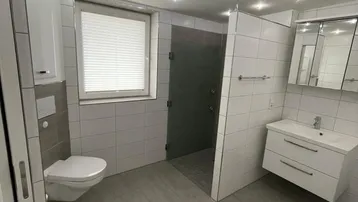 Modernes Badezimmer mit begehbarer Dusche, Wand-WC und Fenster, hell gefliest.