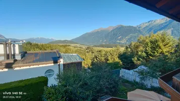 Panoramablick auf die umliegende Berglandschaft und grüne Natur von einem sonnigen Balkon aus.