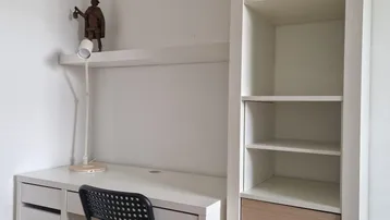 Helles Arbeitszimmer mit weißem Schreibtisch, schwarzem Stuhl und hohem Regal mit Schubladen.