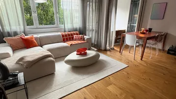 Helles Wohn- und Esszimmer mit Holzboden, beigem Sofa und Zugang zum Balkon.