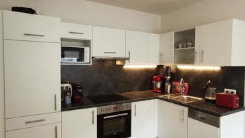 Moderne Küche mit weißen Schränken, dunkler Arbeitsplatte und Holzboden, ausgestattet mit Backofen und Mikrowelle.