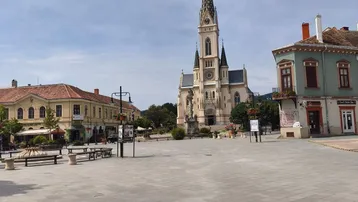 Historischer Stadtplatz mit imposanter Kirche und umliegenden Gebäuden unter blauem Himmel.