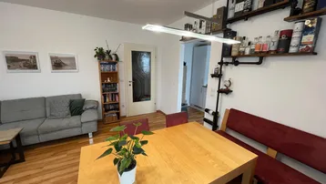 Heller Wohn- und Essbereich mit Holztisch, bequemer Sitzbank und dekorativen Wandregalen.