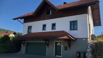 Traditionelles Einfamilienhaus mit Satteldach, integrierter Garage und gepflegter Fassade unter blauem Himmel.