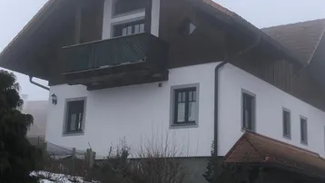 Traditionelles Haus mit Satteldach und Balkon, umgeben von Schnee und Nebel.