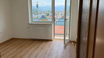 Heller Raum mit Laminatboden und Zugang zu einem Balkon mit Bergblick.
