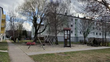 Spielplatz mit Schaukeln und Klettergerüst vor einem Mehrfamilienhaus mit kahlen Bäumen.