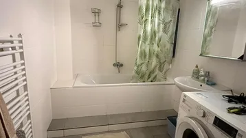 Funktionales Badezimmer mit Badewanne, Duschvorhang, Waschbecken und Waschmaschine.