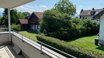 Geräumiger Balkon mit Fliesenboden und Blick ins Grüne, umgeben von Hecken und Bäumen.