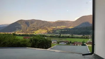 Weitläufiger Blick von einer Dachterrasse über ein grünes Tal mit umliegenden Bergen.