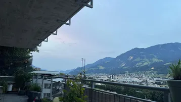 Geräumiger Balkon mit Fliesenboden, Pflanzen und weitem Blick auf die Berge und die Stadt.