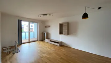 Helles Wohnzimmer mit Parkettboden, weißen Wänden und direktem Zugang zu einem Balkon.
