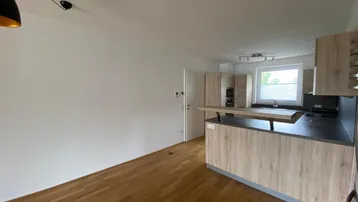 Moderner Küchenbereich mit Holzoptik-Fronten, dunkler Arbeitsplatte und Frühstücksbar.