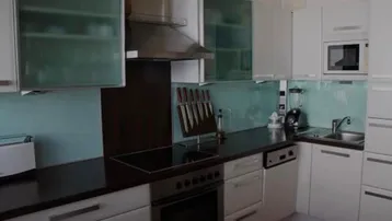 Moderne Küche mit weißen Schränken, dunkler Arbeitsplatte und blauer Rückwand.