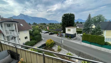Blick vom Balkon mit Sitzgelegenheiten auf eine Straße und die umliegende Berglandschaft.