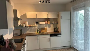 Moderne Einbauküche mit hellen Fronten, Holzarbeitsplatte und Zugang zum Balkon.