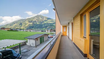Langer Balkon mit Fliesenboden und weitem Blick auf die umliegende Berglandschaft und grüne Wiesen.
