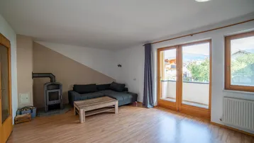 Helles Wohnzimmer mit Laminatboden, gemütlichem Schwedenofen und Zugang zum Balkon.