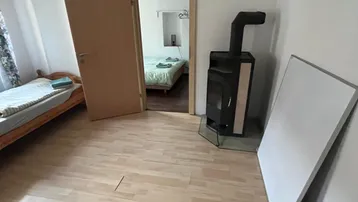 Helles Zimmer mit Holzboden, einem Einzelbett und einem gemütlichen Holzofen, der zu einem weiteren Schlafzimmer führt.