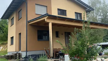 Modernes zweistöckiges Haus mit zweifarbiger Fassade, überdachter Terrasse und gepflegtem Gartenbereich.