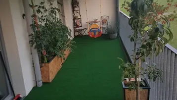 Langer Balkon mit Kunstrasen, Pflanzen und einer Schaukel, bietet einen grünen Ausblick.