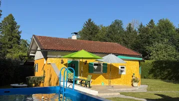 Gelbes Haus mit rotem Dach, umgeben von einem grünen Garten und einem oberirdischen Pool.