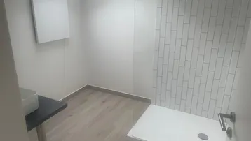 Modernes Badezimmer mit Duschbereich, Waschbecken, hellem Boden und Oberlicht für natürliches Licht.