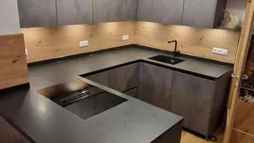 Moderne Küche mit grauen Fronten, schwarzer Arbeitsplatte und Holzakzenten.