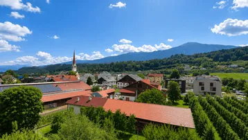 Panoramablick über eine malerische Stadt mit Kirche, grünen Feldern und majestätischen Bergen im Hintergrund.