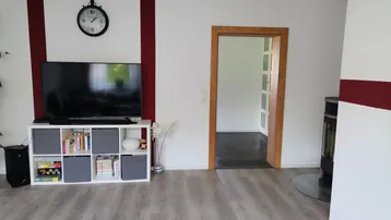 Gemütliches Wohnzimmer mit Fernseher, modernem Kaminofen und hellem Laminatboden.