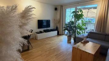 Helles Wohnzimmer mit Holzboden, gemütlichem Sofa und Zugang zum Balkon.