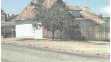 Einfamilienhaus mit Satteldach, einem Baum im Vorgarten und einer Holzumzäunung an einem sonnigen Tag.