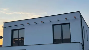 Modernes Gebäude mit weißer Fassade und dunklen Fenstern bei Sonnenuntergang.