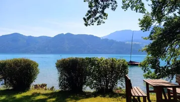 Idyllischer Gartenbereich mit Holztisch und Bänken, direkt am See mit Bergblick.