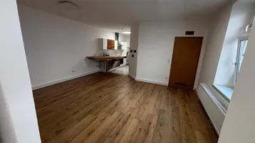 Heller offener Wohnbereich mit Holzboden und Blick in die moderne Küche, ideal für geselliges Beisammensein.
