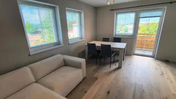 Helles Wohn- und Esszimmer mit Holzboden, beigem Sofa und Zugang zum Balkon.