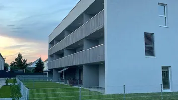 Moderne Wohnanlage mit Balkonen und gepflegter Rasenfläche bei Sonnenuntergang.