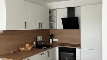 Moderne Küche mit weißen Schränken, Holzoptik-Arbeitsplatten, schwarzer Spüle und integriertem Backofen.