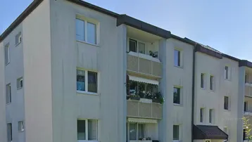 Mehrfamilienhaus mit heller Fassade, Balkonen und gepflegter Grünfläche im Vordergrund.